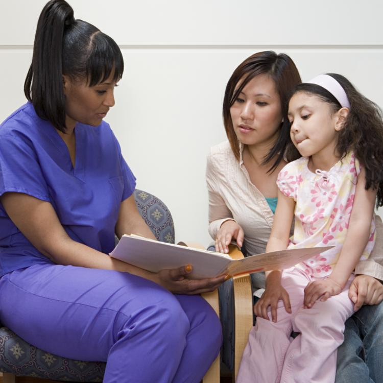 Nurse wearing purple scrubs talking to mom and daughter